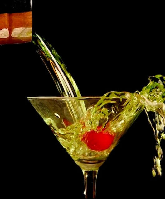 Pouring a drink into a martini glass with a cherry in it